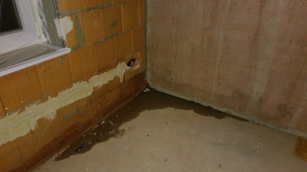 Kellerraum unter Bau mit Wasserpfütze am Boden, feuchte Wand und offenes Mauerwerk