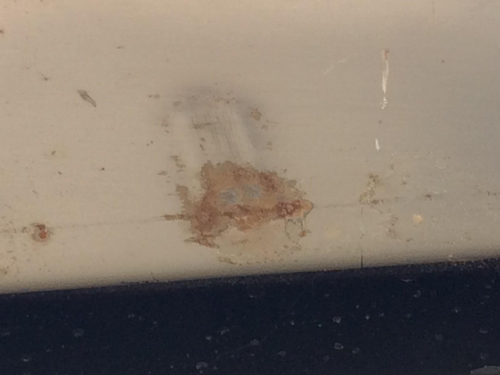 Weiße Wand mit rostbraunem Fleck und Abplatzungen am unteren Rand