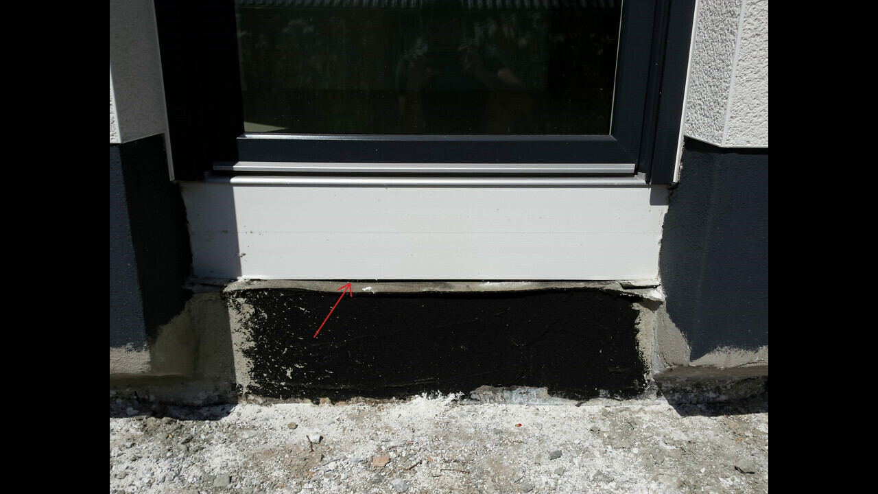 Außenbereich eines Fensterrahmens über dunklem Fundament mit beschädigter Abdichtung.