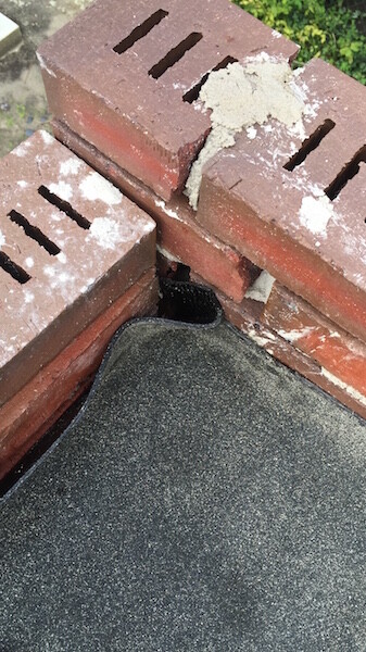 Nahaufnahme von Ziegelmauerwerk mit Mörtelresten und Dachabdichtungsmaterial