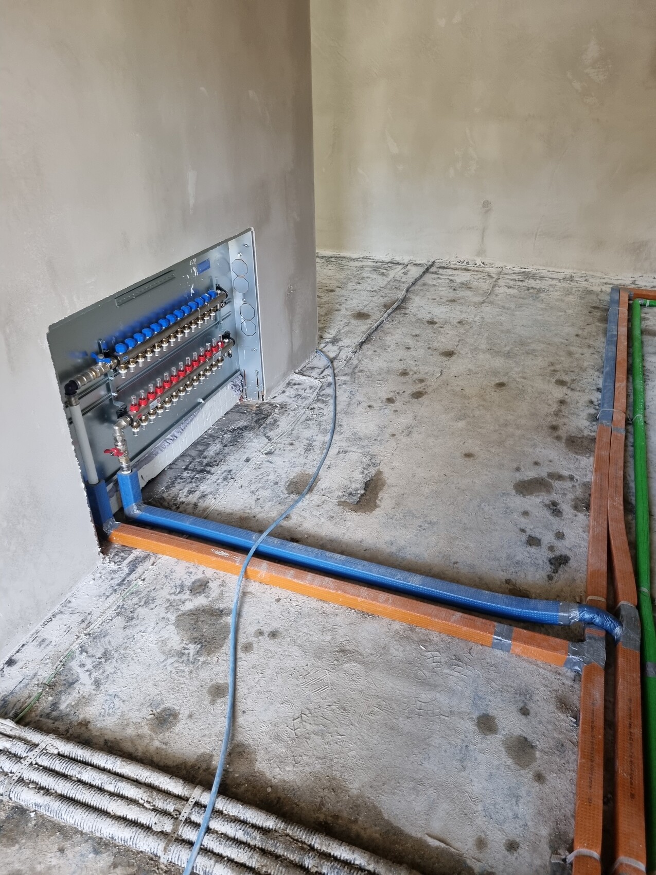 Offener Verteilerschrank mit blauen/roten Anschlüssen; Kabel- und Rohrleitungen auf dem Bauboden.