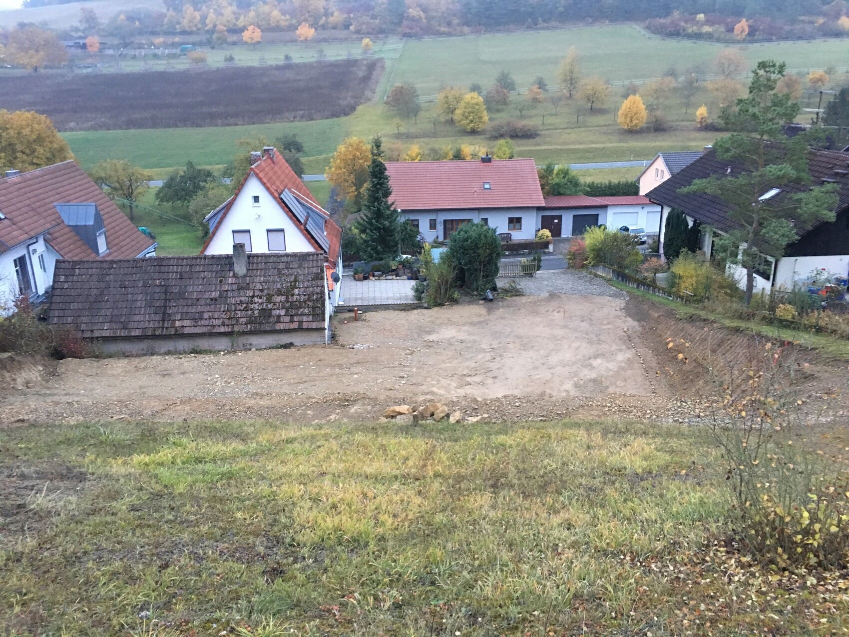 Hügeliges Dorf mit freiem Bauplatz und angrenzenden Häusern, Herbstfarben.
