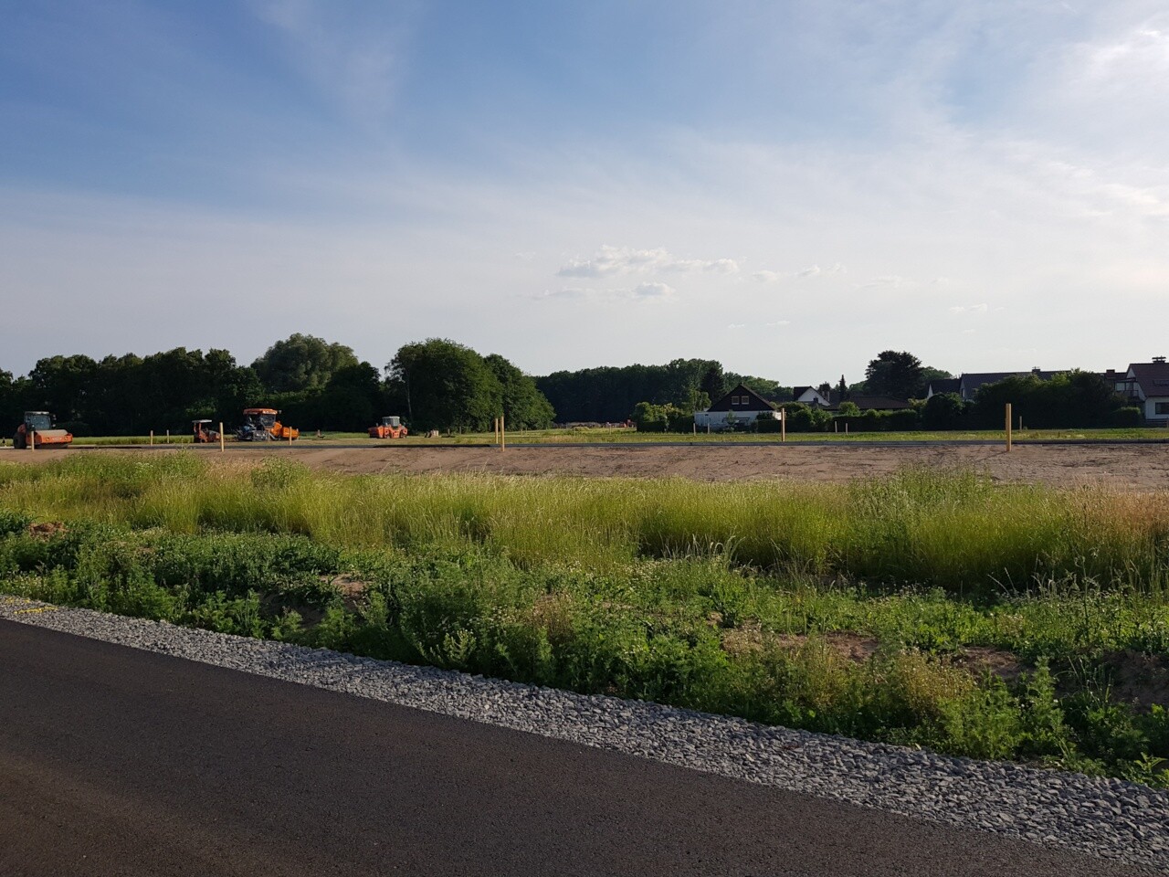 Bauplatz mit Baumaschinen auf freier Grundstücksfläche, Hintergrund Häuser und grünem Gras