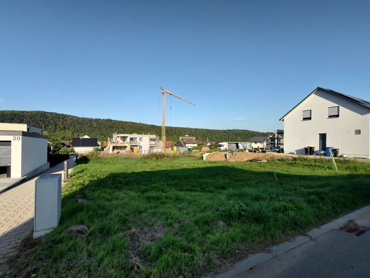 Bauplatz mit Kran und Neubauten, grüne Wiese im Vordergrund, blauer Himmel.