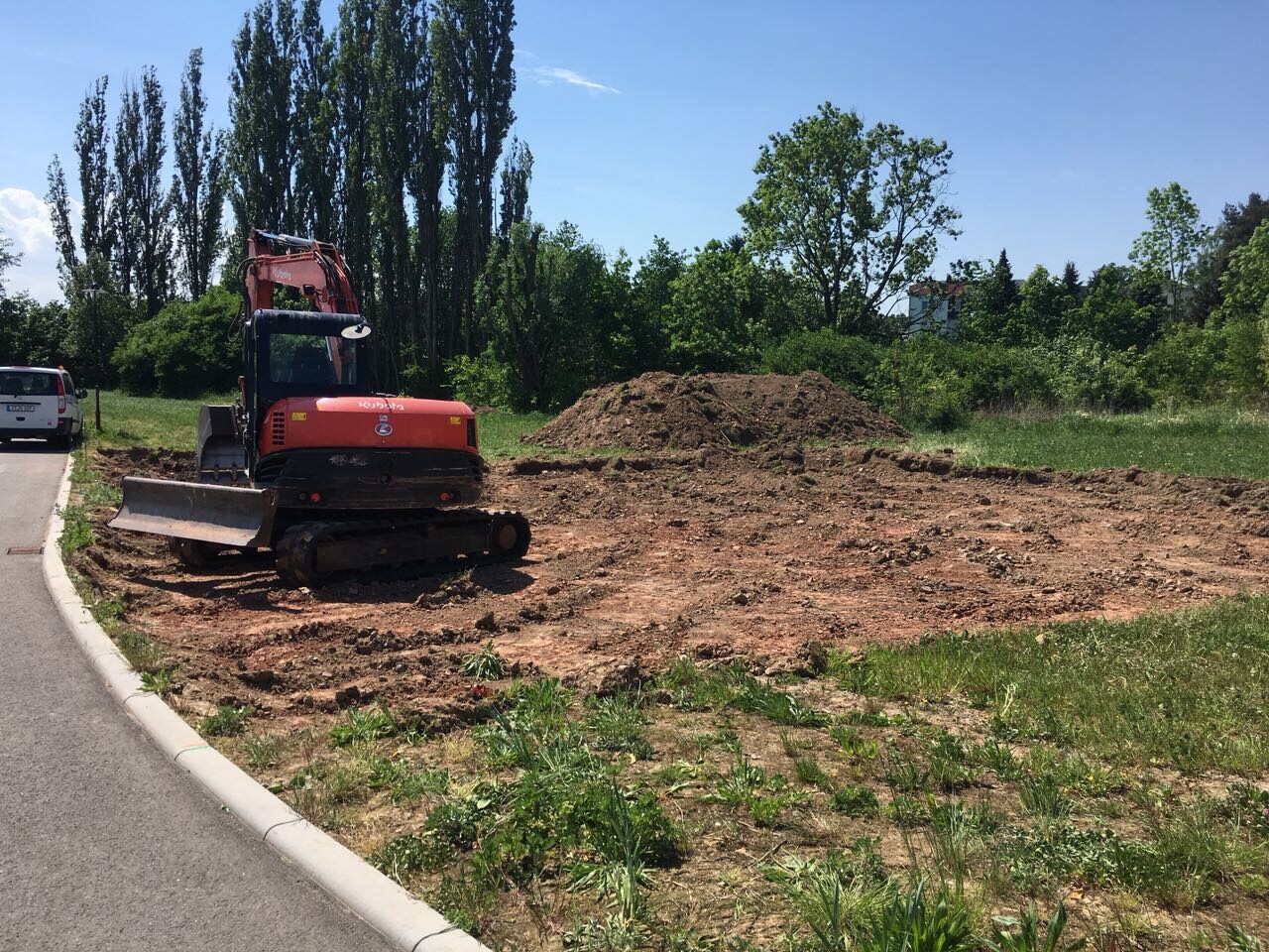 Kleiner roter Minibagger auf Bauplatz mit Erdhaufen und Bäumen im Hintergrund