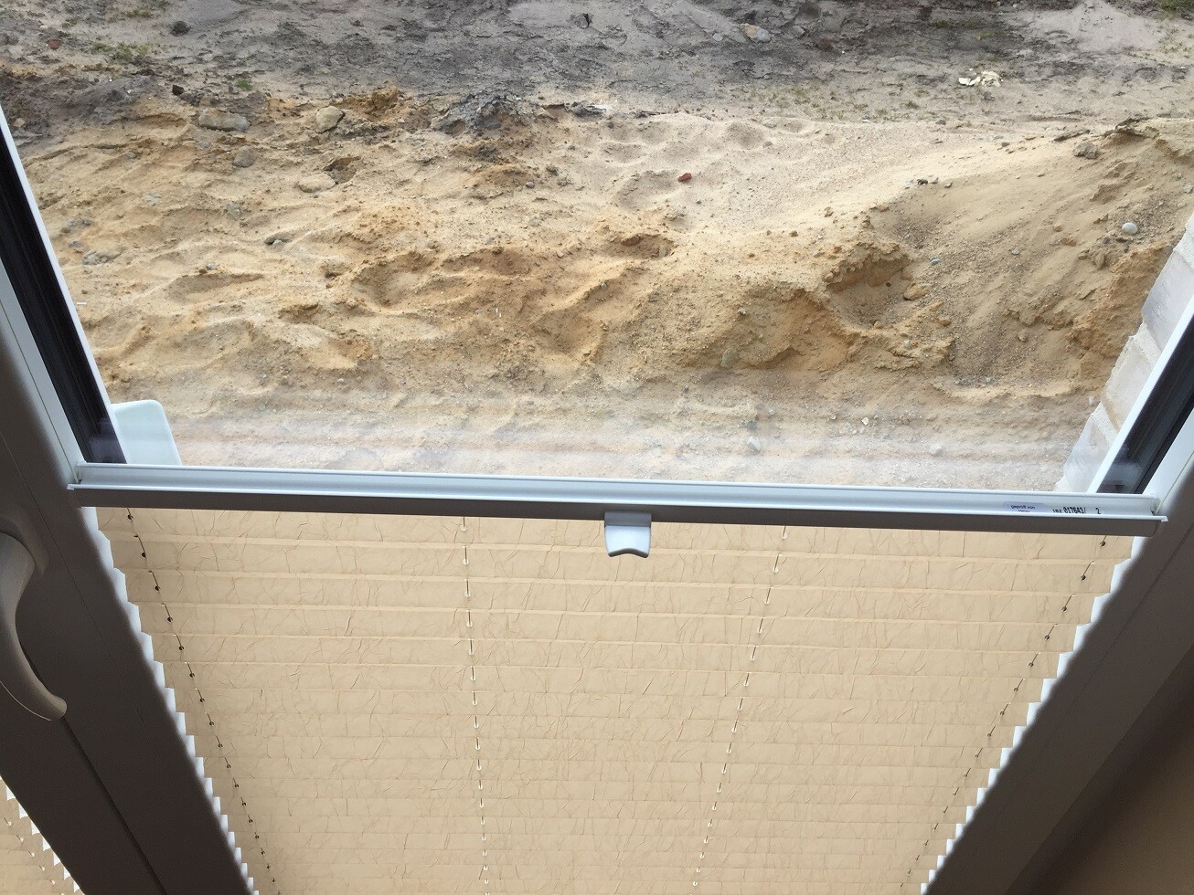 Blick von innen durch Fenster mit Jalousien auf Sand und Erdreich eines Bauplatzes