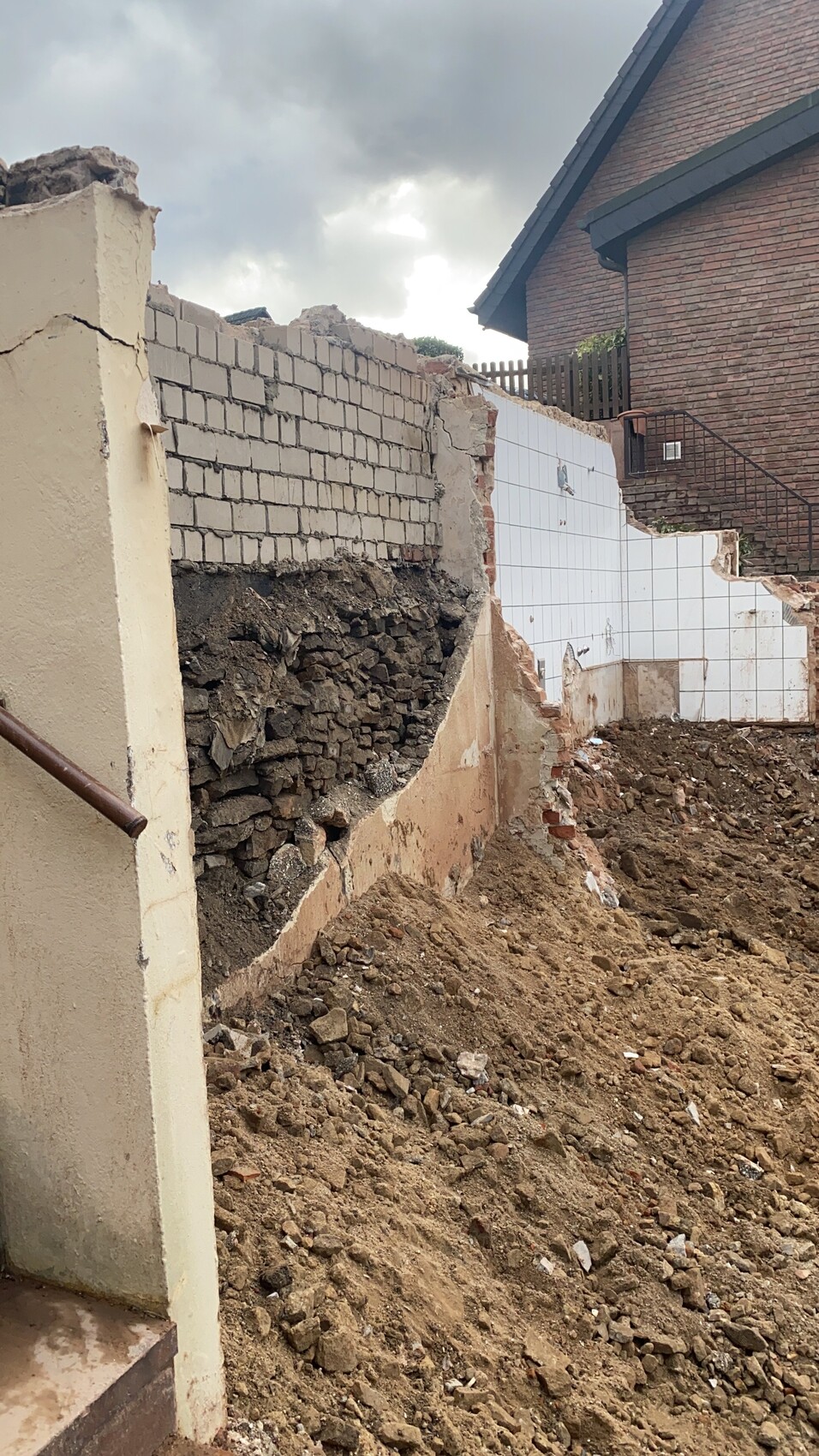 Abgerissene Mauerreste, Erdmassen und Kies neben einem Haus - Baustelle mit Schutt.