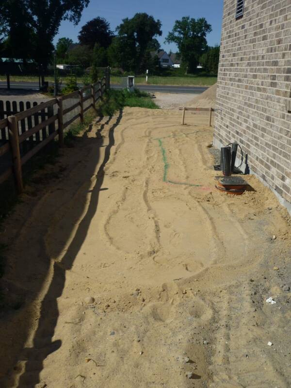 Sandboden neben Hauswand; Kreidemarkierungen, Spuren im Sand, Zaun links