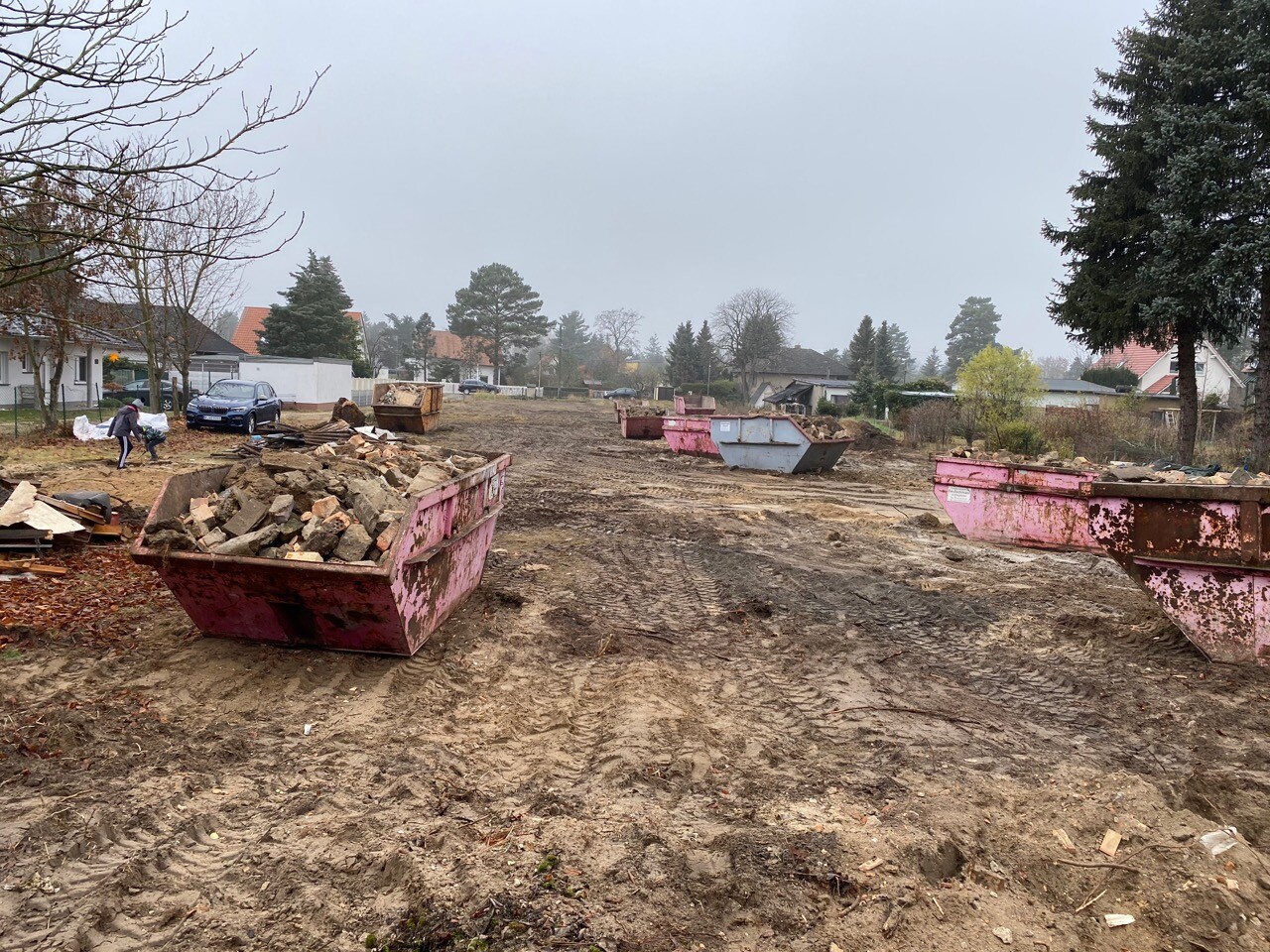 Baustelle im Vorort mit pinken Containern voller Geröll und Matsch.