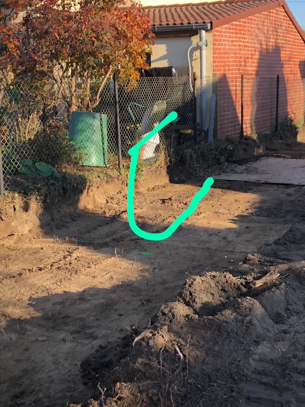 Baustelle im Freien mit Graben, Drahtzaun, Baucontainer und Backsteingebäude im Hintergrund.