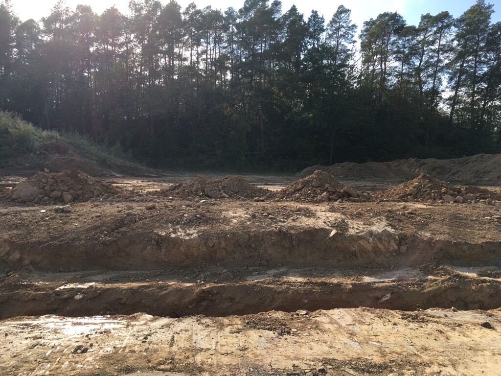 Baustelle mit großen Erdarbeiten, Gräben und Erdmassen, Wald im Hintergrund