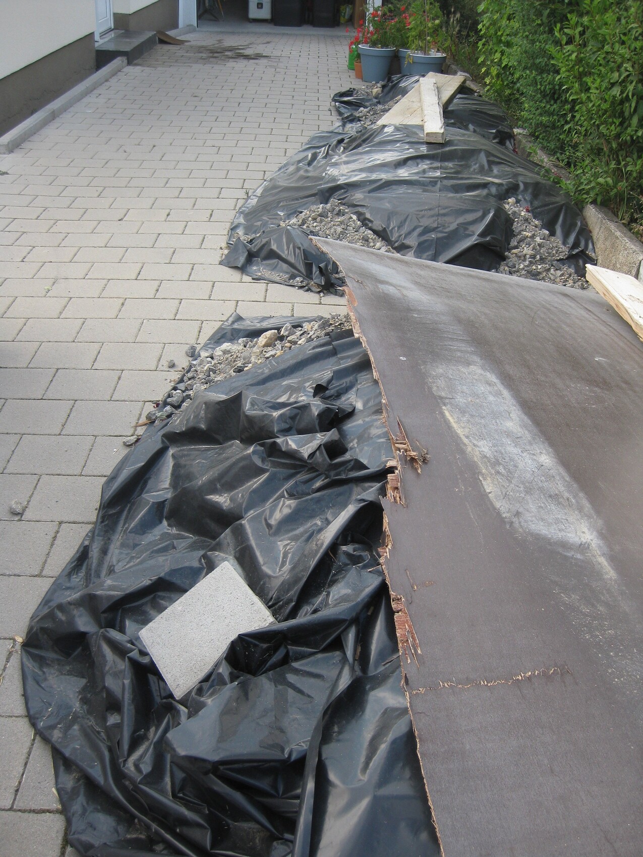 Gehweg mit schwarzen Planen, Geröll, Brettern und Bauabfällen einer Baustelle.