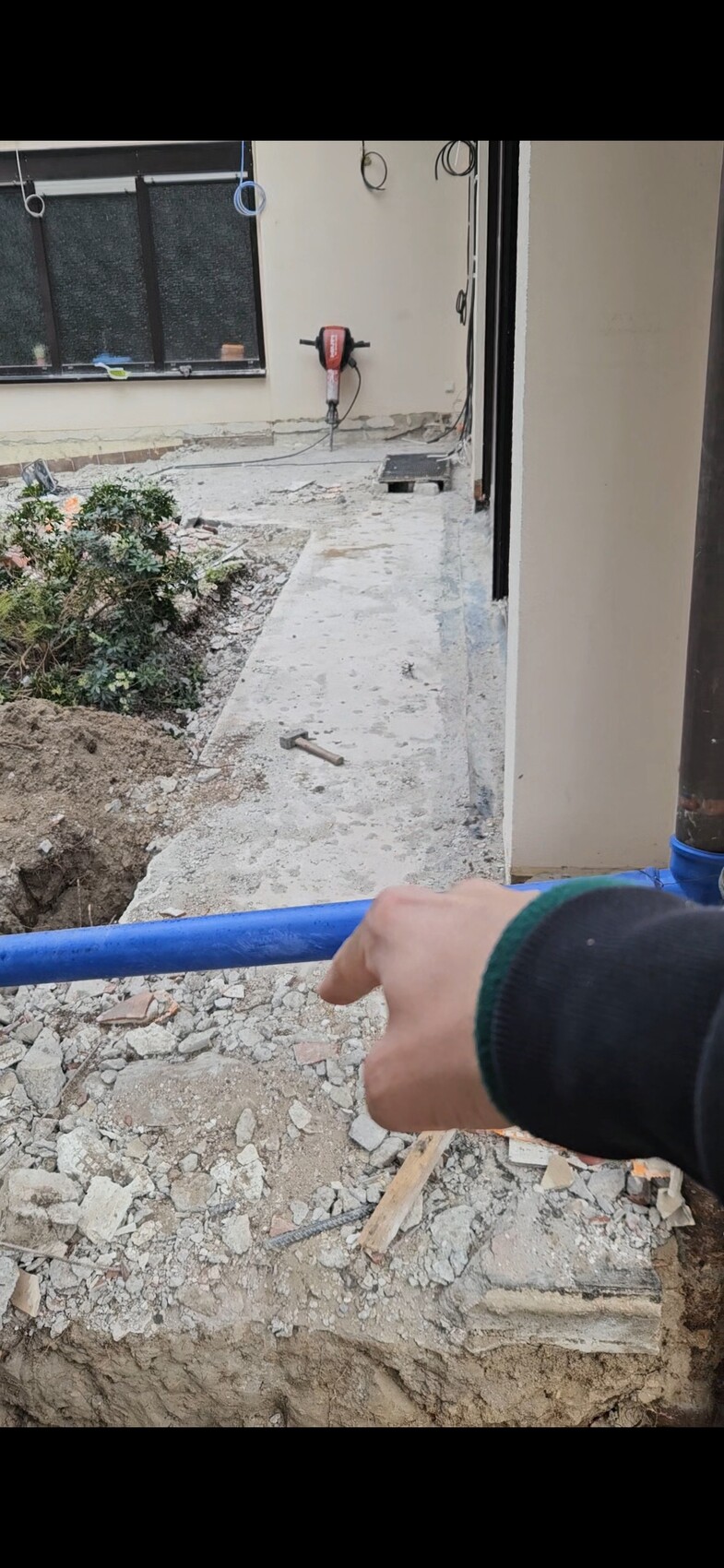 Bauarbeiten im Innenhof: Hand hält blaues Rohr, Baugerätschaften und Trümmer im Hintergrund.