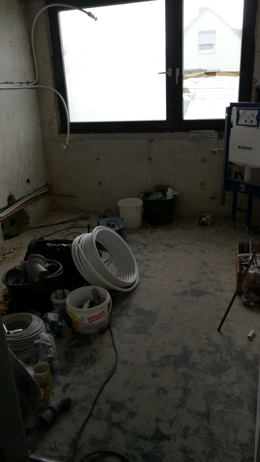 Unfertiges Badezimmer mit Fenster, Sanitärinstallationen, Rohre und Baumaterialien.
