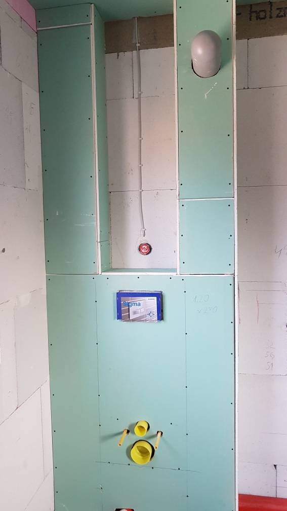 Grüne Trockenbauwand im Bau mit Rohren, Schachtöffnung und Messgerät.