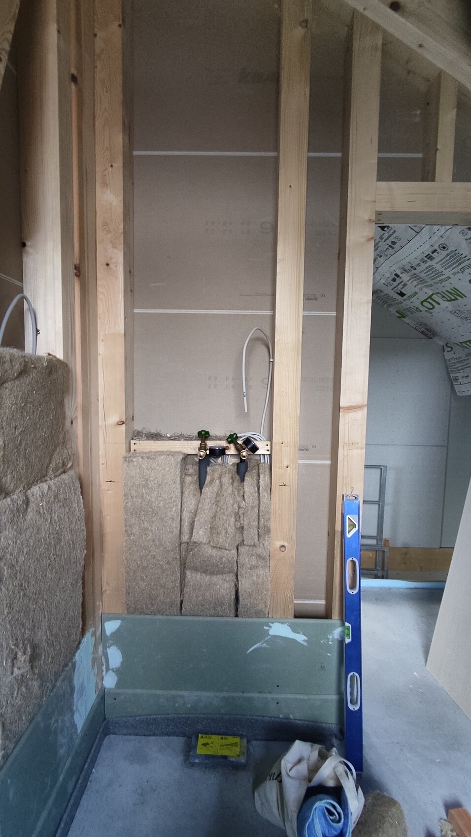 Unfertige Badezimmerwand mit Holzrahmen, Wasserleitungen, Ventil-Armaturen und Dämmmaterial.