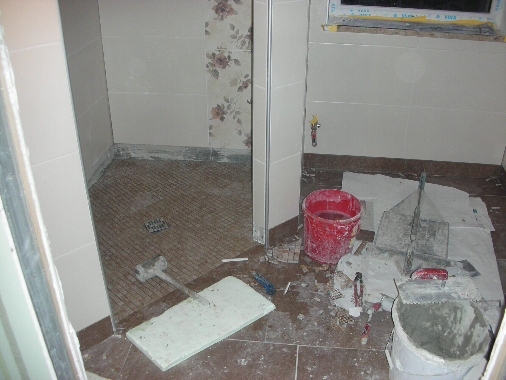 Badezimmer im Renovierungszustand mit Eimer, Fliesenboden, Werkzeugen und Putzmaterial.