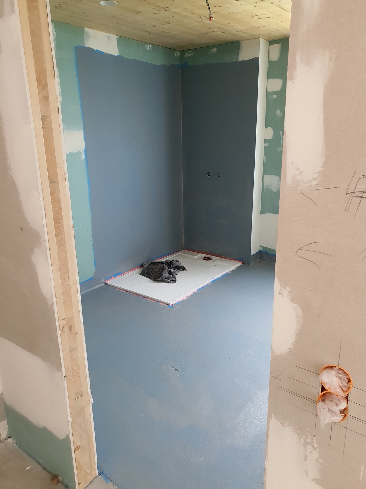 Badezimmer-Baustelle: blaue Dichtbeschichtung an Wänden, Duschwanne mit rotem Rand.