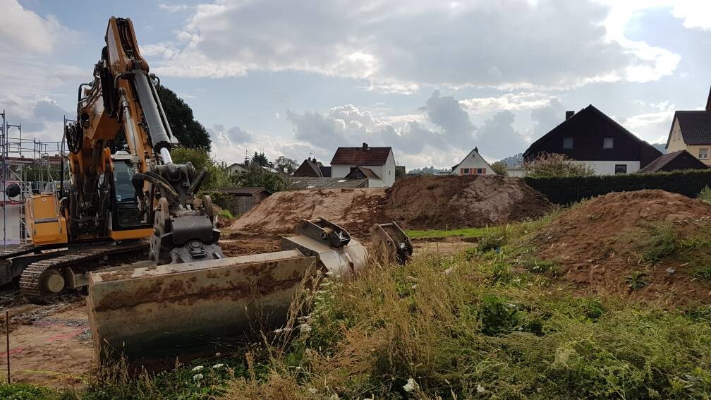 Großer Bagger auf Baustelle mit Erdaushub und Häusern im Hintergrund
