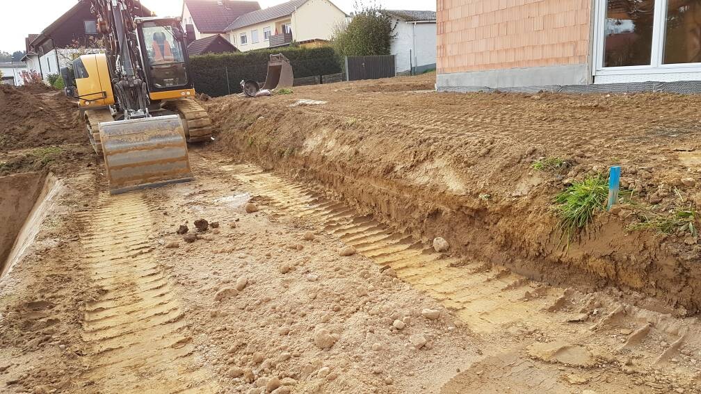 Bagger gräbt langen Graben auf Baugrundstück neben einem Wohnhaus.