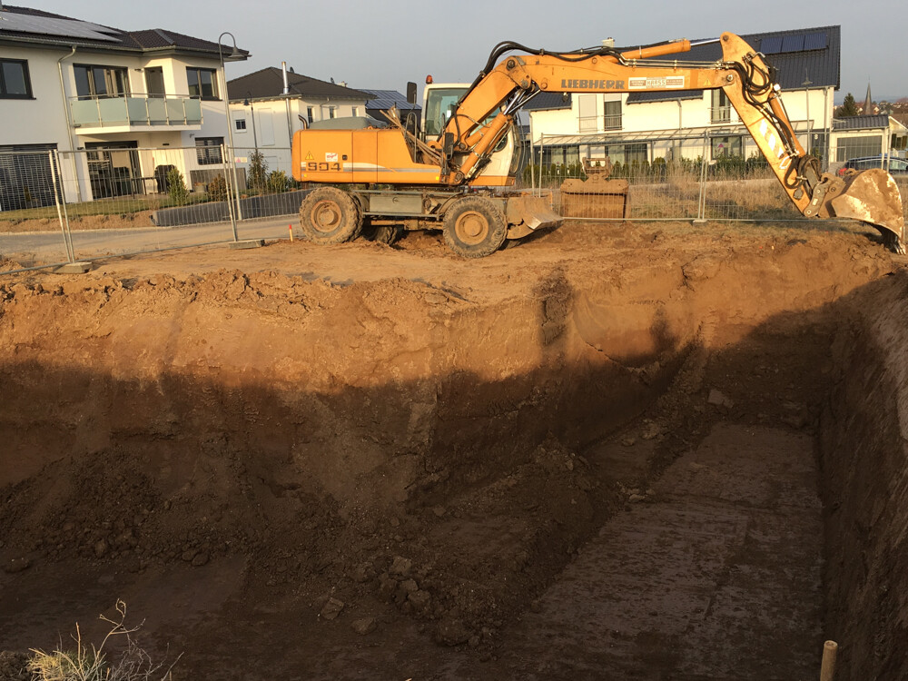 Bagger auf einer Baustelle gräbt eine Baugrube; Wohnhäuser im Hintergrund