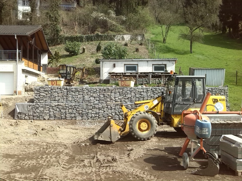 Baustelle mit gelbem Frontlader, Betonmischer, Steinmauer und Baugeräten.