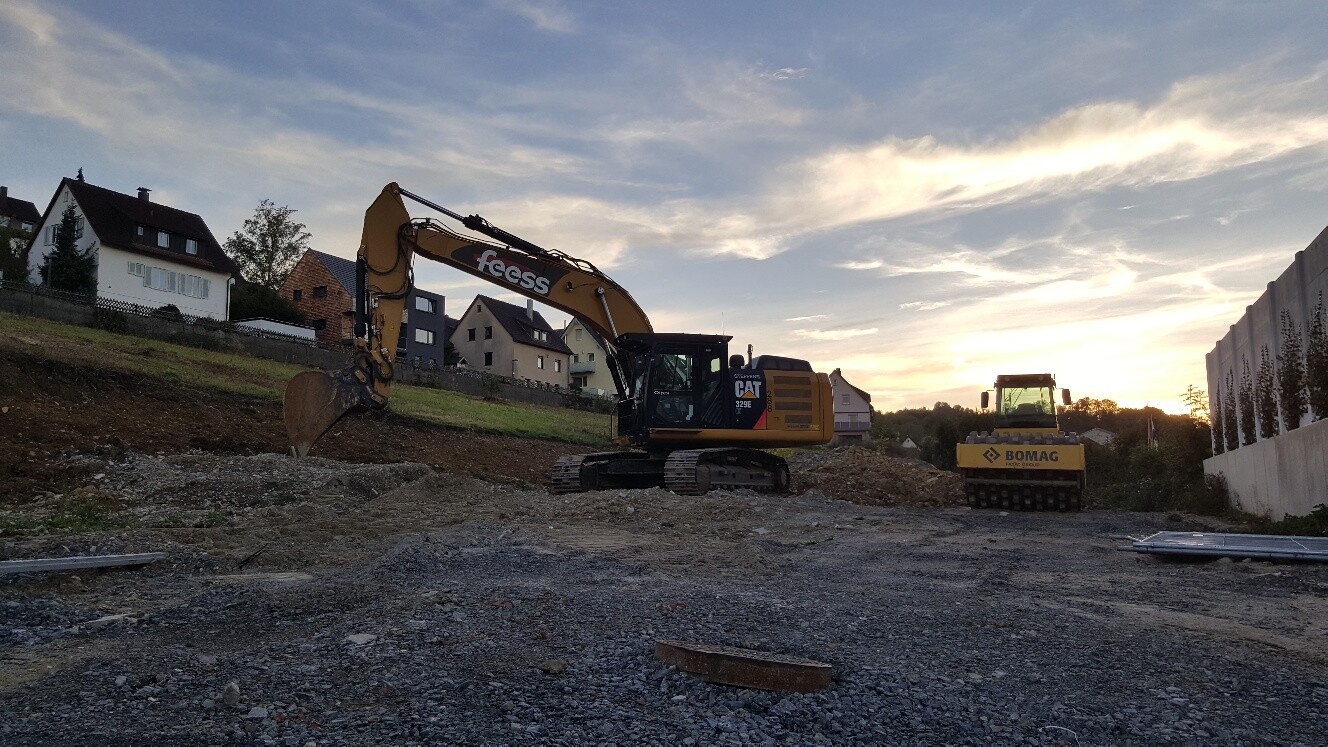 Baustelle mit Bagger und Erdbau, Häuser im Hintergrund bei Sonnenuntergang