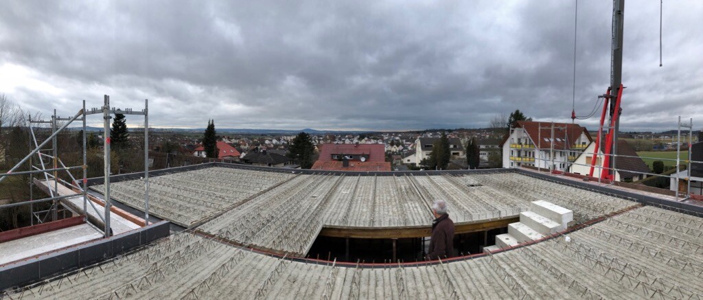 Person steht auf Dach mit Stahlbewehrung; Baugerüst, Kran, städtische Skyline im Hintergrund