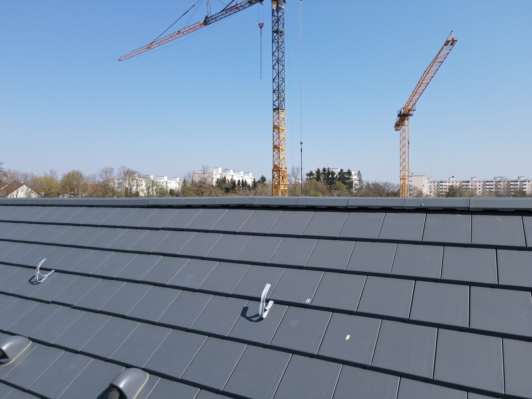 Dach mit dunkelgrauen Ziegeln, Baukräne im Hintergrund auf einer Baustelle