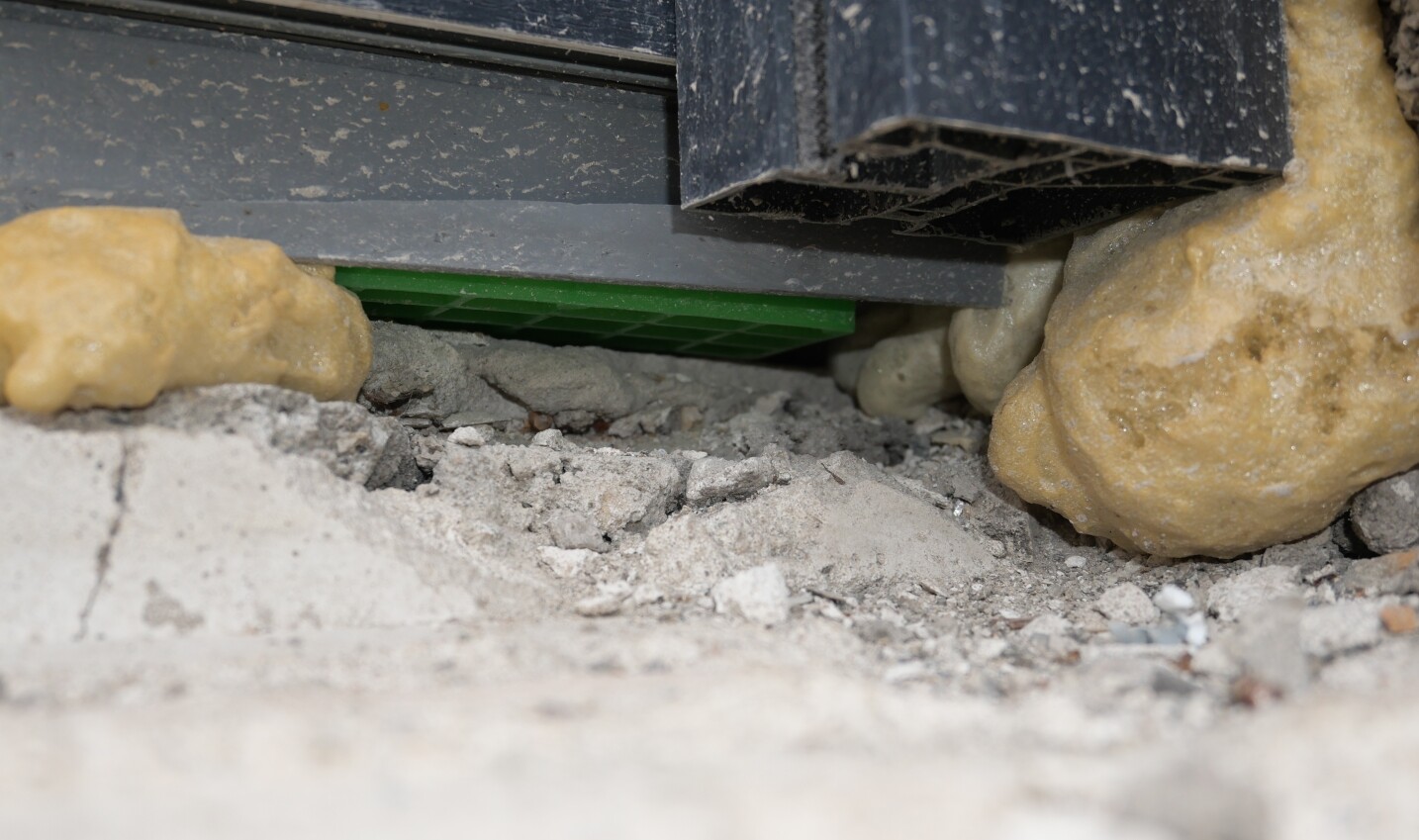Baustellenboden mit Staub und Kies, Gelber Dämmstoff, schwarzes Metallprofil, grüne Leiste.