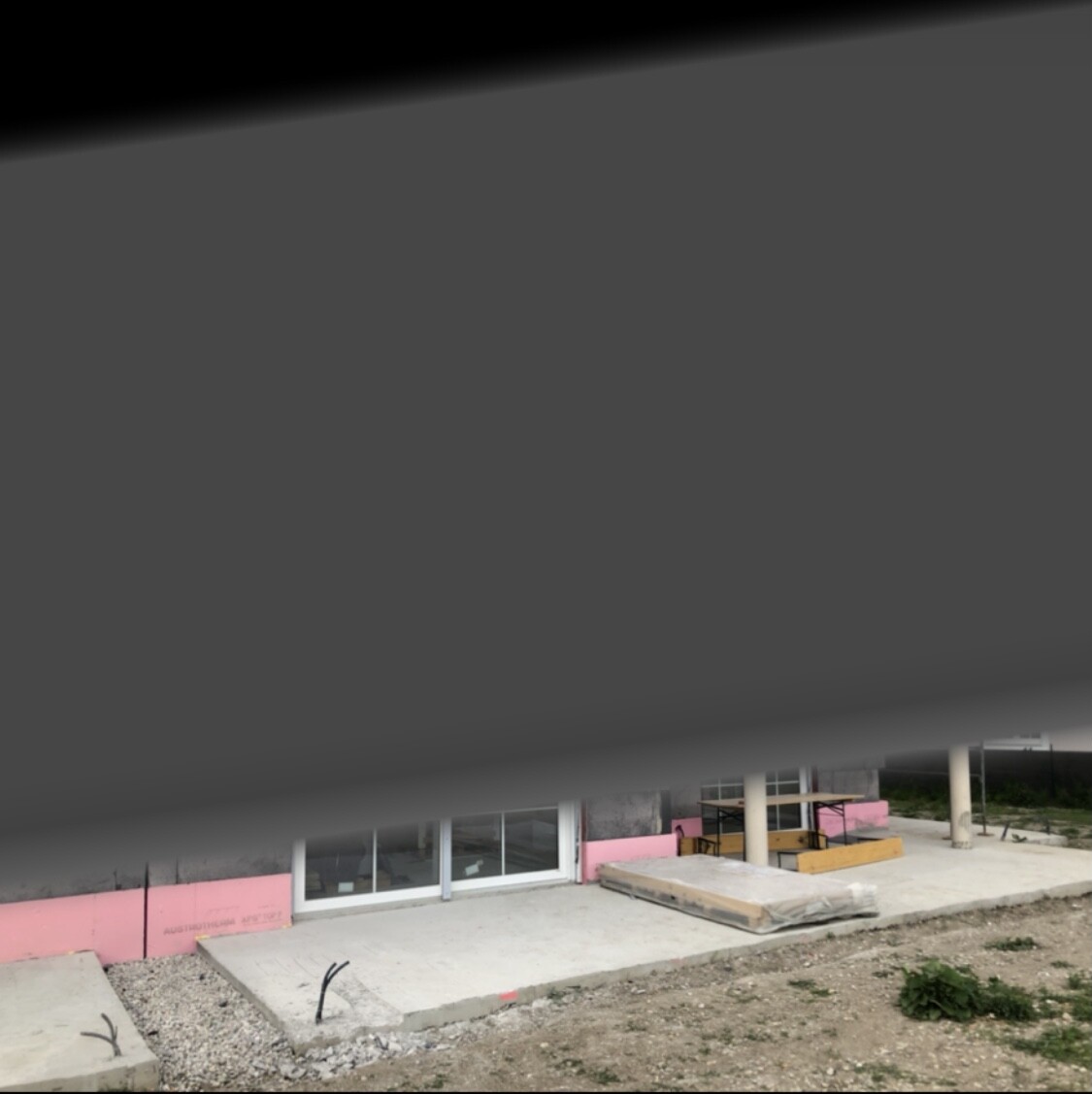 Baustelle am Gebäude: Glasfront, pinke Dämmplatten, Betonboden und Erde davor.
