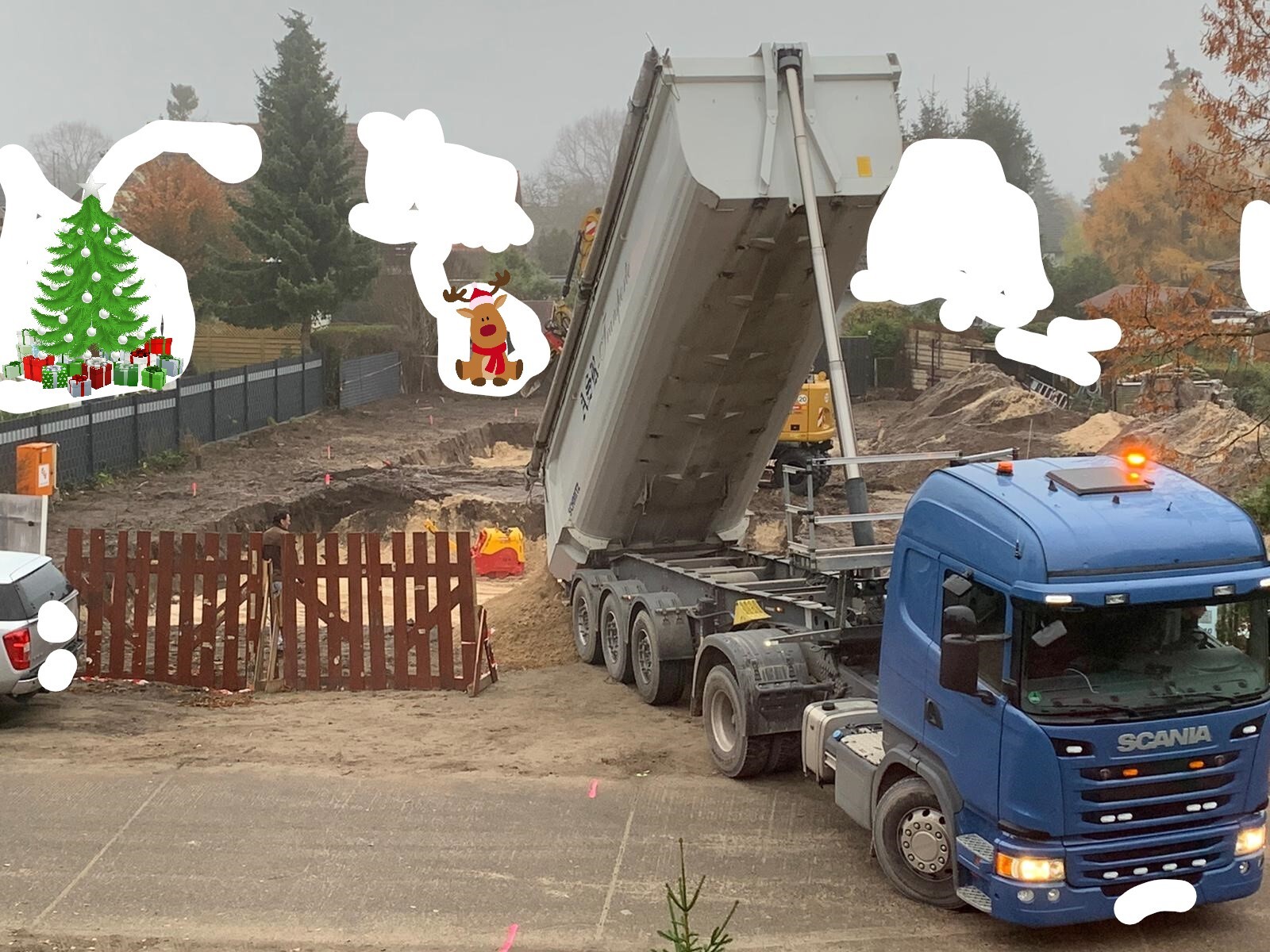 Baustelle: blauer Scania-LKW kippt Sand aus dem Anhänger, Bauzäune sichtbar
