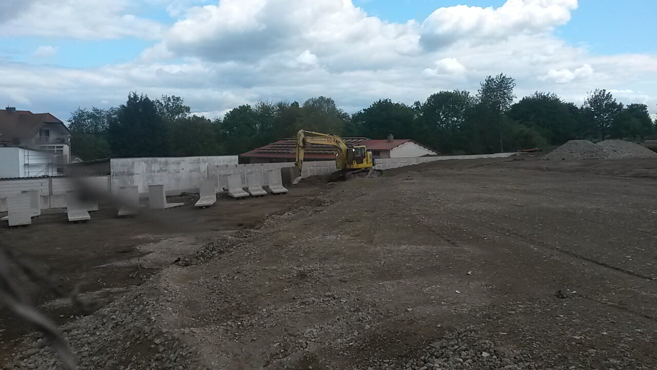Gelber Bau-Exkavator auf einer Baustelle mit Betonbarrieren, Erde und Bäumen im Hintergrund
