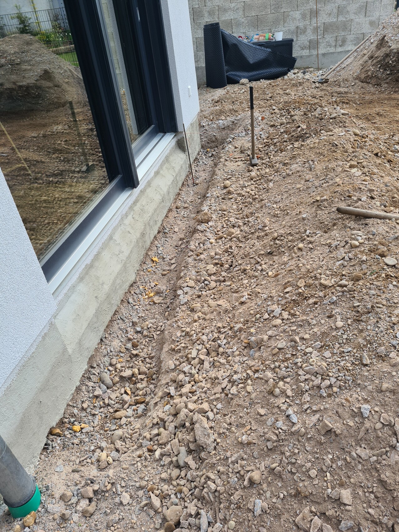 Baustelle am Haus: Graben entlang der Glasfassade, Kies, Erde und Spaten im Boden.