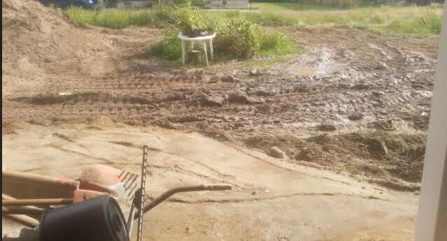 Schlammige Baustelle mit Erdarbeiten, Bauwerkzeugen und einem Stuhl im Hintergrund