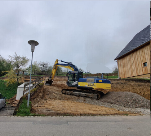 Bagger auf einer Baustelle neben einem Rohbau-Untergrund und Erdaushub im Gelände.