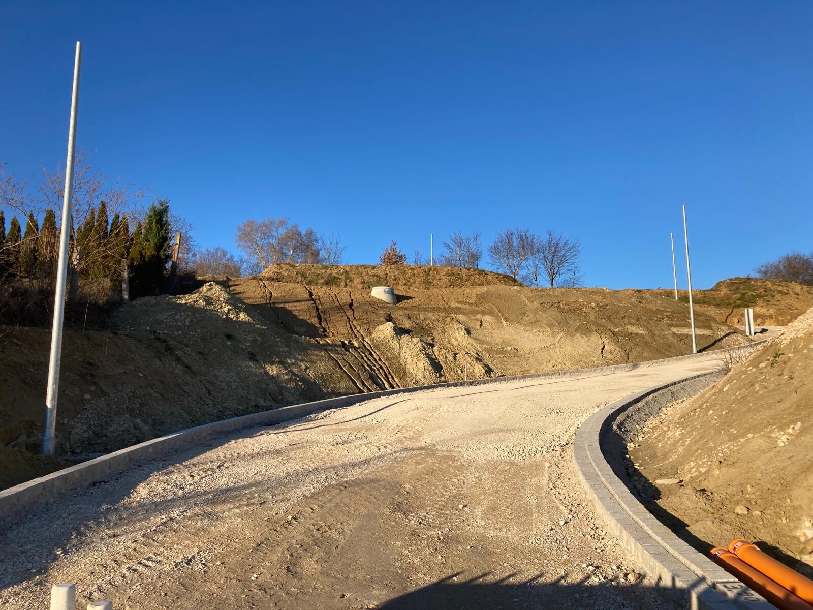 Unbefestigte Baustellenstraße, Kurvenführung, Erdmassen, Pfosten, blauer Himmel.