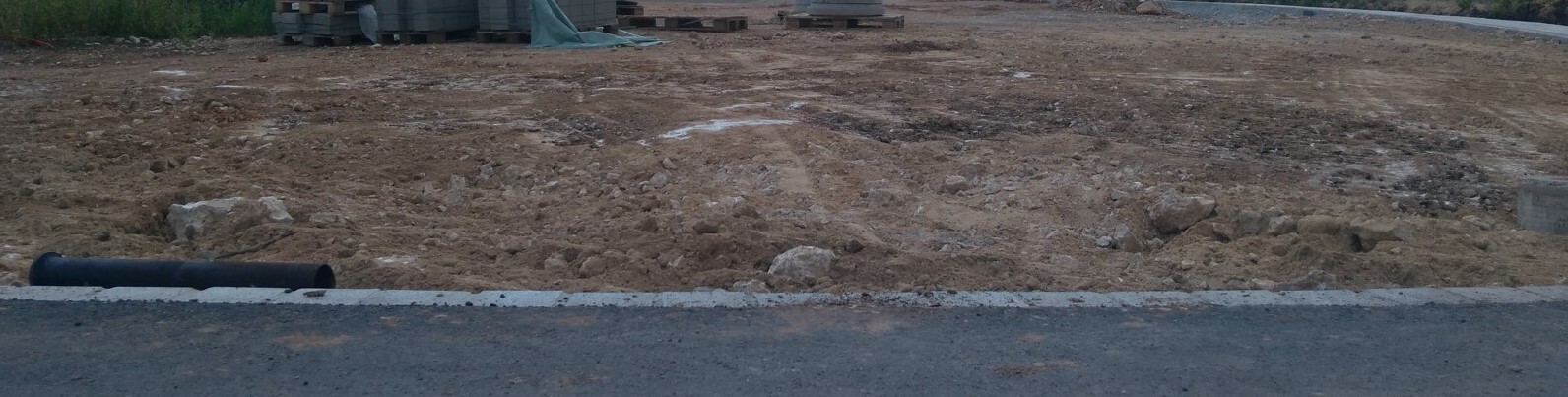 Baustelle mit Erdreich, lose Steine und schwarzes Rohr neben Asphaltkante.