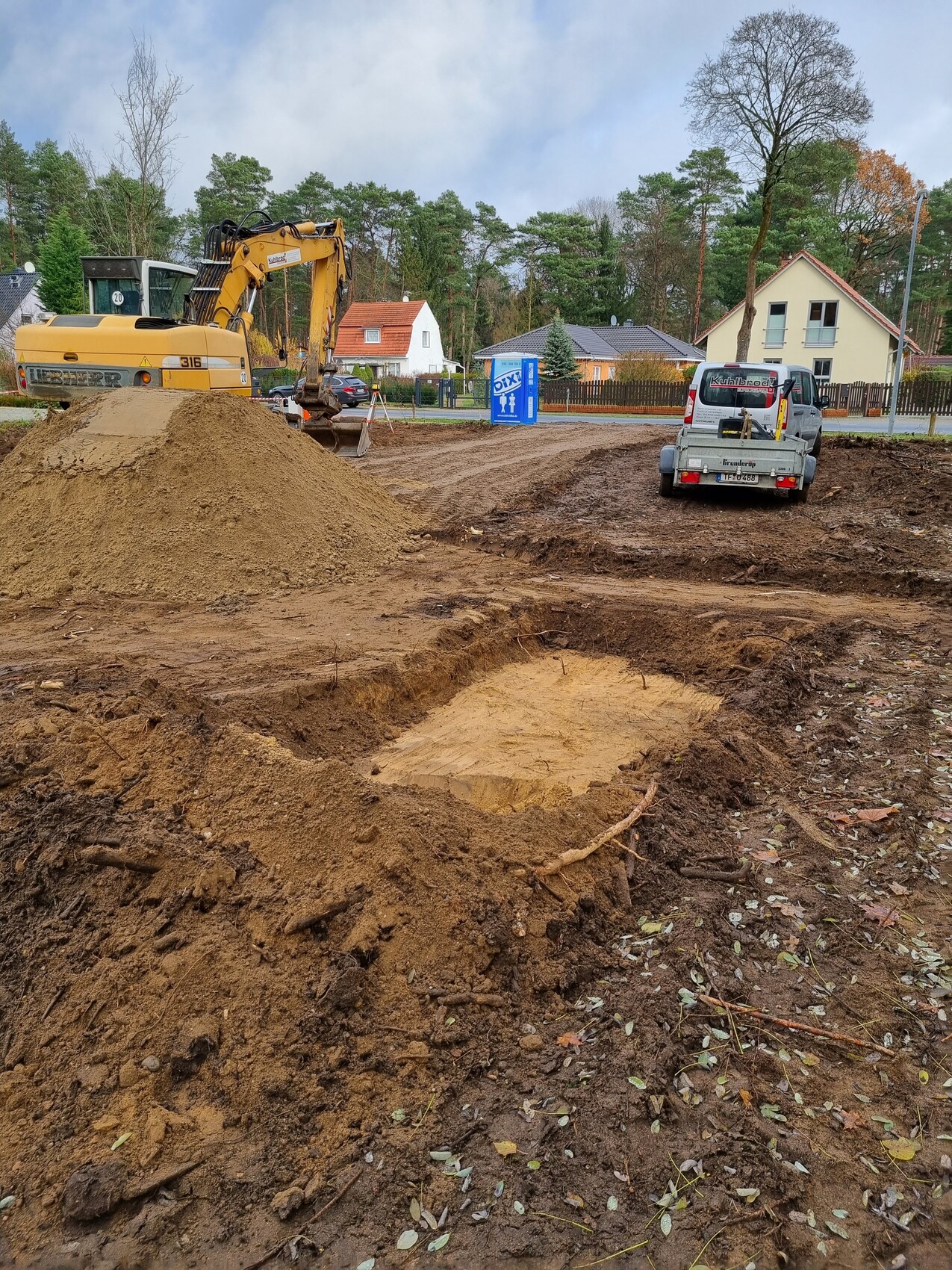 Baustelle mit Bagger, Erdmassen und kleinem Wagen; blaues DIXI-Klo im Hintergrund.