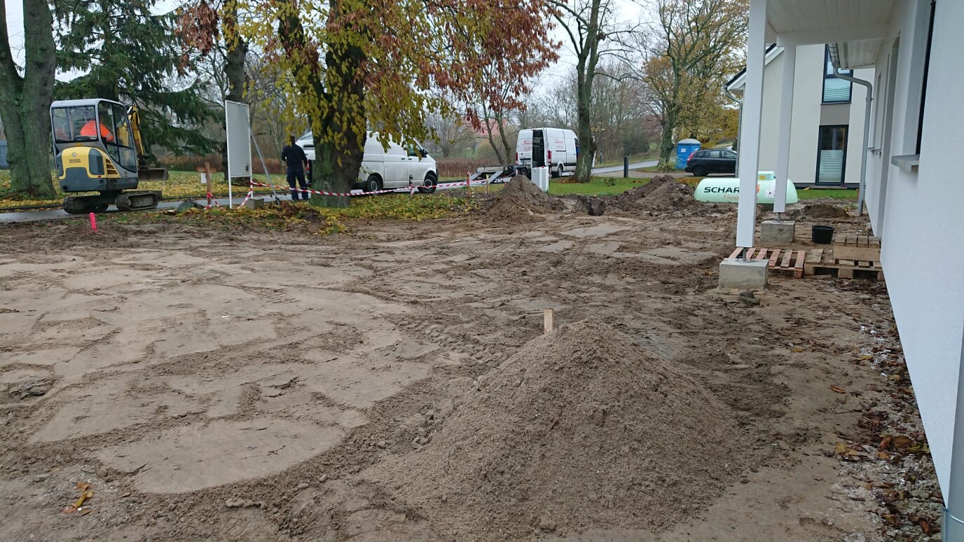 Bauarbeiten auf Grundstück: Erdaushub, Mini-Bagger links, Absperrband, Van im Hintergrund.