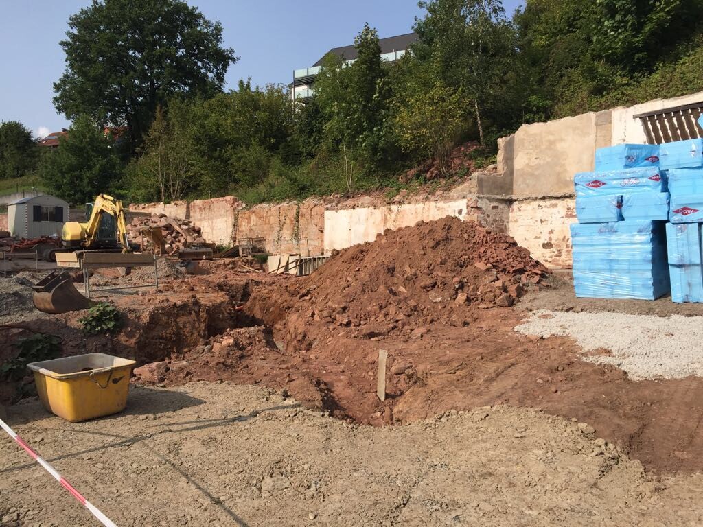 Baustelle mit Bagger, Erdhaufen und Baumaterialien für Rohbau und Fundament