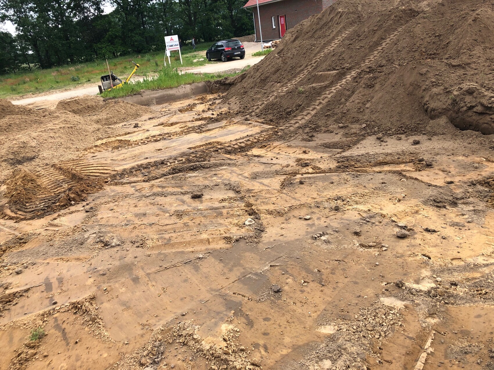 Baustelle mit großen Erdmassen, Spuren von Baumaschinen im Schlamm, Sandhügel im Hintergrund.