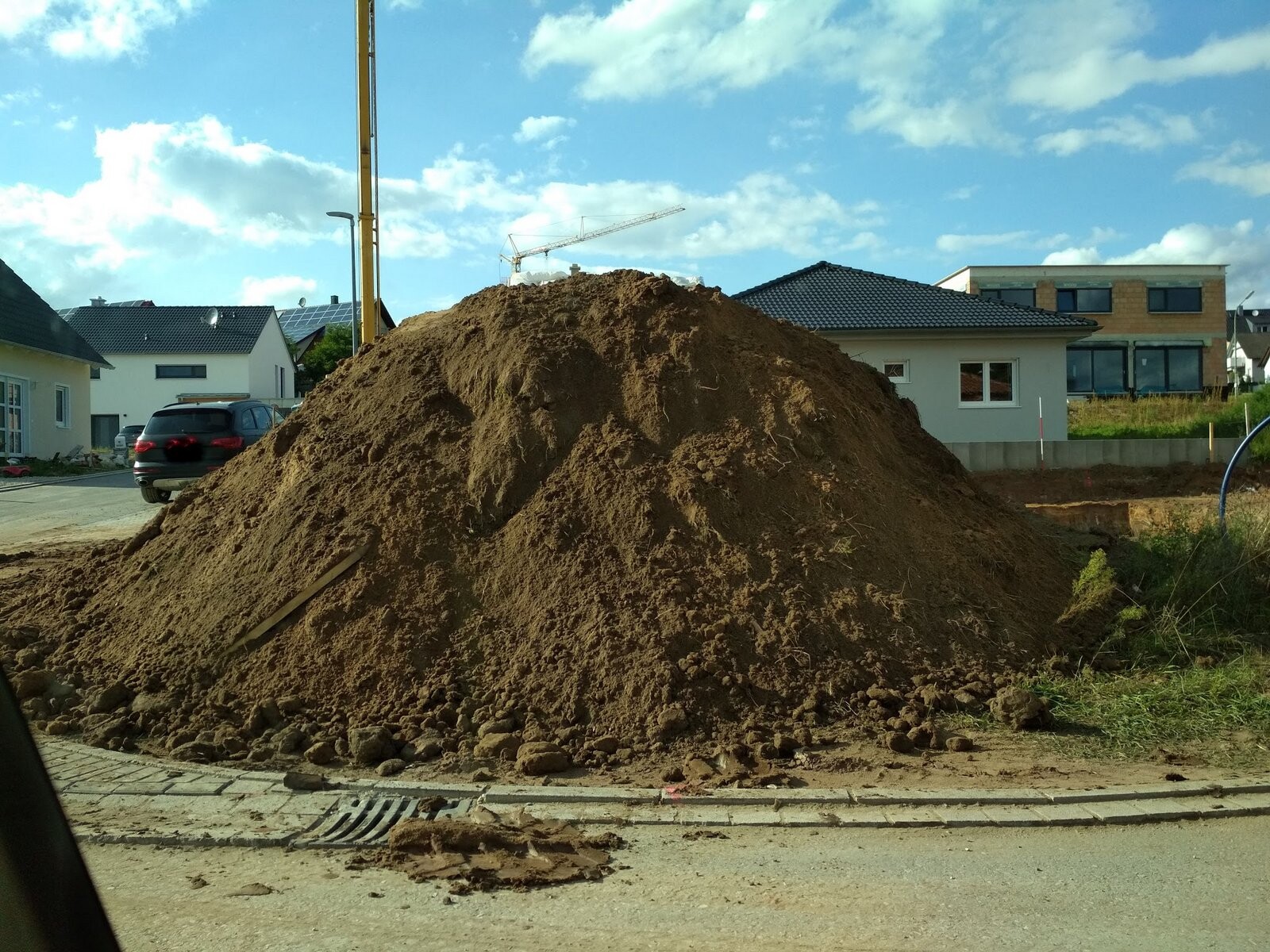 Großer Erdhaufen auf einer Baustelle vor Wohnhäusern mit Kran im Hintergrund.