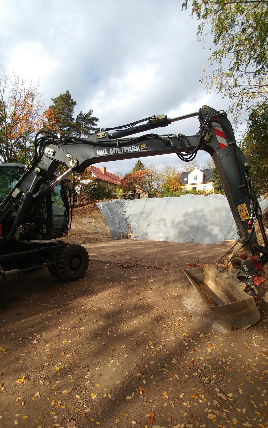 Großer Baggerarm auf Baustelle mit Herbstlaub, Hintergrund Häuserlandschaft