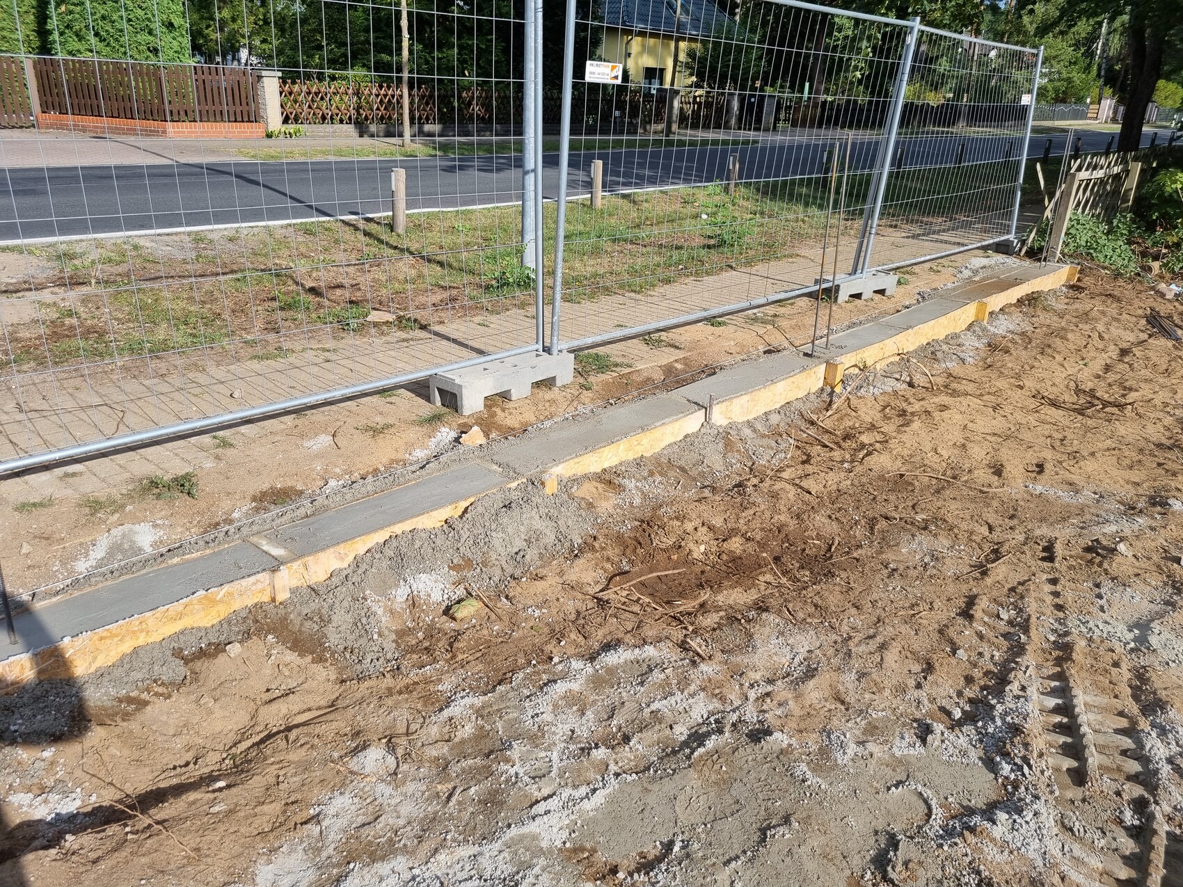 Baustelle am Gehweg: provisorischer Metallzaun, Erdarbeiten, Kies und Schutt.