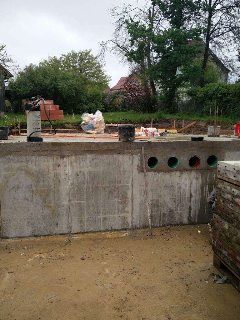 Baustelle mit Betonfundament, runden Öffnungen, Bauholz und Materialien; Bäume im Hintergrund