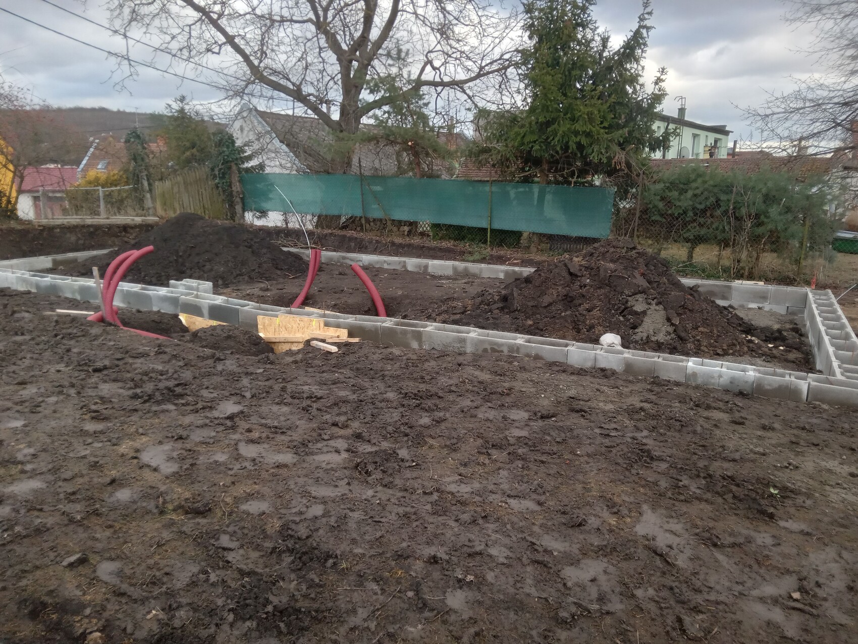 Baustelle mit Fundament aus Betonblöcken, Erdreich und roten flexiblen Rohren.