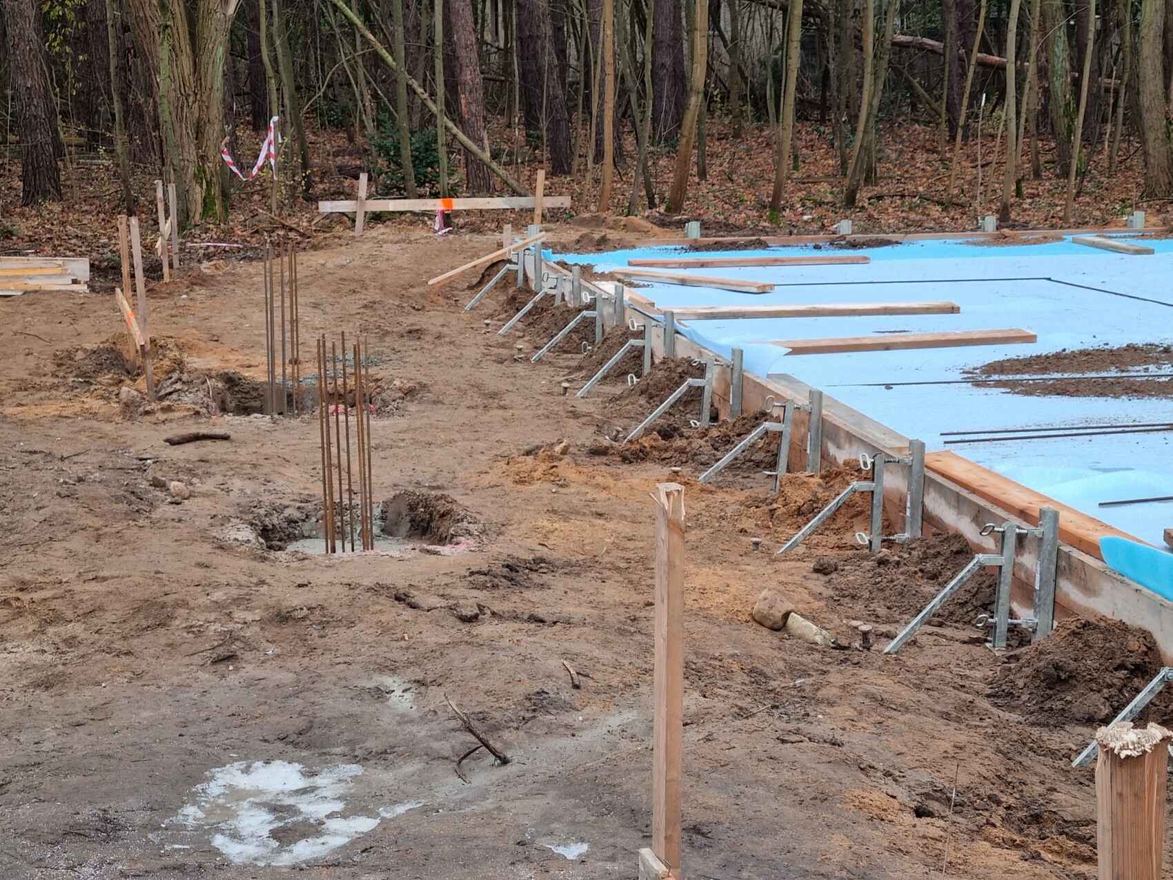 Baustelle im Wald: Graben mit Stahlarmierung, blau abgedeckte Fundamentplatte und Metallstützen