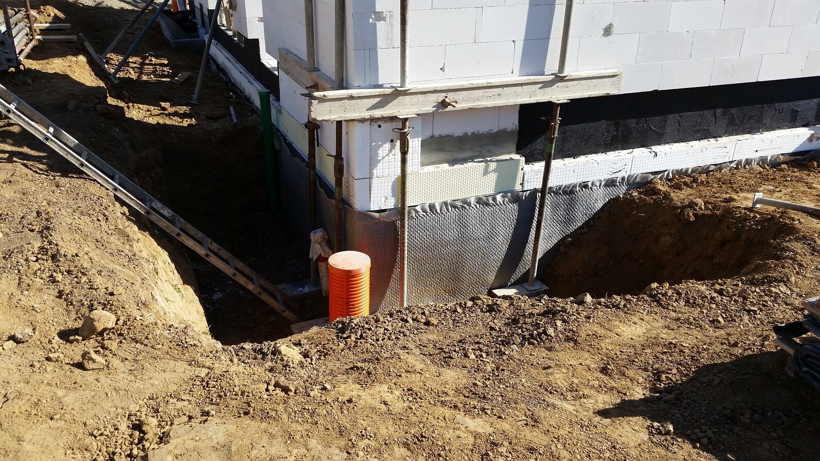 Baustelle mit Fundamentwand, Stützen und Erdarbeiten am Neubau