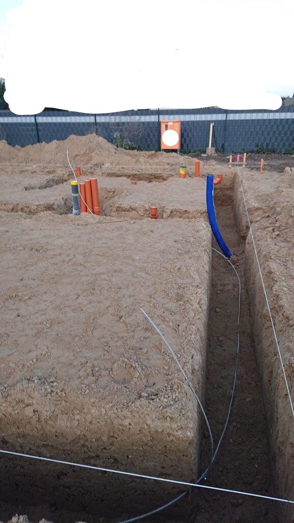 Offene Baugrube auf einer Baustelle mit blauer Rohrleitung, Kabeln und Erdarbeiten.